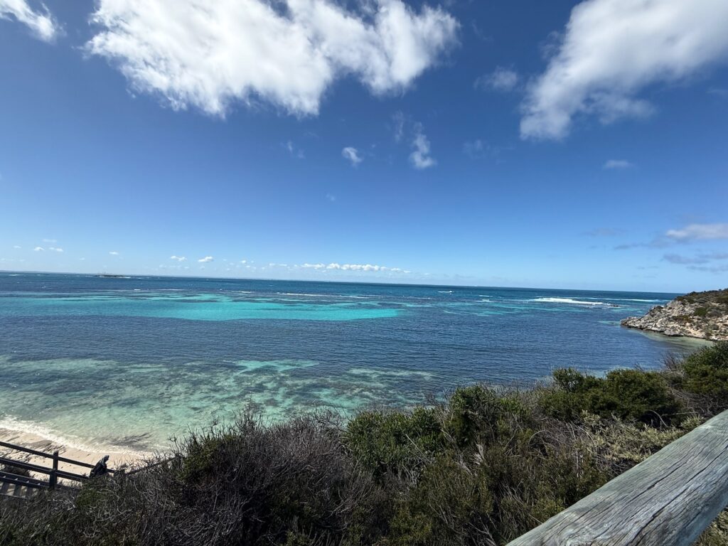 Dark coral and sand under clear blue sea water, and blue sky with a few clouds