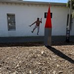 Artwork on side of the museum showing an action figure of a bare-chested Indigenous man in ragged white trousers, one arm and hand raised, the other facing towards the ground, perhaps as if about to throw an invisible weapon.