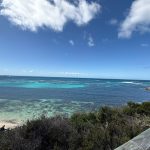 Dark coral and sand under clear blue sea water, and blue sky with a few clouds
