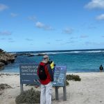 Doug, wearing a red coat, hat and backpack, reads an information sign in front of Little Salmon Bay at Parker Point