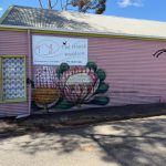 Large scale painting of a bee, a banksia, and a Waratah on the pink wall of "The House Paddock", a homewares store next to the toilets