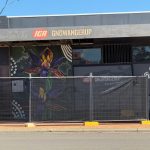 A beautiful flower mural on the side of an IGA store, unfortunately partly obscured by a wire fence